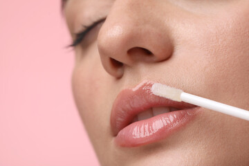 Woman applying lip gloss on pink background, closeup. Space for text