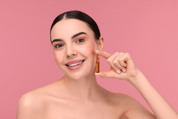 Obraz na płótnie Canvas Beautiful young woman holding skincare ampoule on pink background