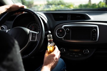 Driver driving a car with a bottle of alcohol in his hands close-up.