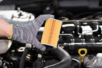 Auto mechanic changes oil filter for diesel cars, holds new oil filter in his hands against background engine compartment, close-up. Concept replacing auto parts, servicing car in car service center - obrazy, fototapety, plakaty