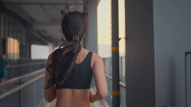 Rear view of young asian woman runner is training in the summer sunset within a city, The athlete fit and firm girl exercising by jogging workout sport outdoor for her healthy wellness.