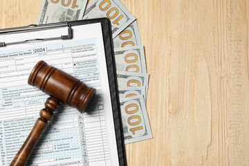 Clipboard with tax return form, gavel and dollar banknotes on wooden table, flat lay. Space for text