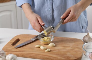 Woman squeezing garlic with press at white table indoors, closeup - obrazy, fototapety, plakaty