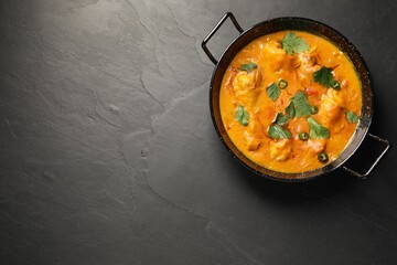 Tasty chicken curry with parsley and pepper on black textured table, top view. Space for text