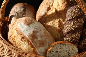 Wicker basket with different types of fresh bread on dark background, closeup