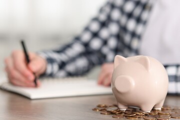 Financial savings. Man writing down notes at wooden table, focus on piggy bank and coins
