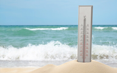 Thermometer in sand near sea showing temperature, summer weather