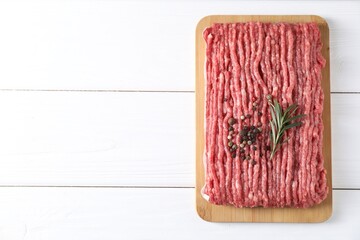 Raw ground meat, rosemary and peppercorns on white wooden table, top view. Space for text