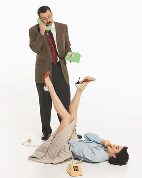 Positive and relaxed young woman lying on floor while man in suit standing and talking on phone. Diversity of emotions. Concept of retro and vintage, fashion, communication, business and lifestyle