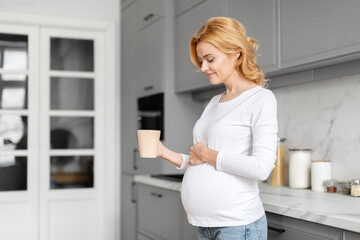 Smiling pregnant woman with a cup in the kitchen