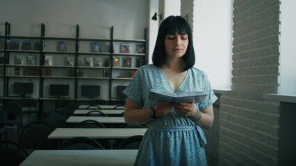 Engrossed woman reading book standing in a library. Informative portrait with depth of field. Continuous learning and research concept. Design for educational poster, banner. Medium shot with blurred