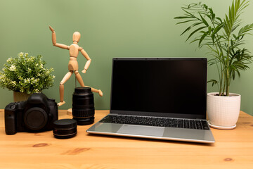 Laptop, camera, lenses and flowers in pots on the desktop.