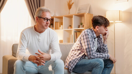 Family misunderstanding. Diverse generation. Relatives quarrel. Offended frustrated dad and son feeling embarrassed after conflict sitting sofa home interior.