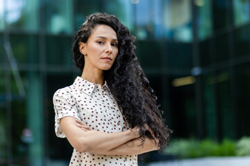 Portrait of serious confident hispanic woman outside office building, businesswoman looking...