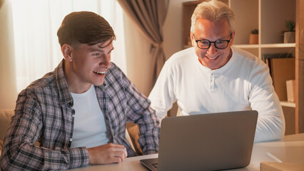Family leisure. Internet bidding. Online auction. Happy father and son watching football sport game together at laptop home interior. - 787227487