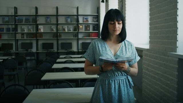 Woman reading a book in a well-lit library. Educational environment portrait. Lifelong learning and information accessibility concept. Design for brochure, educational materials. Medium shot with