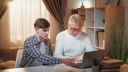 Supportive son. Laptop lesson. Family education. Angry father trying to get information how use computer from son home interior. - 787228216