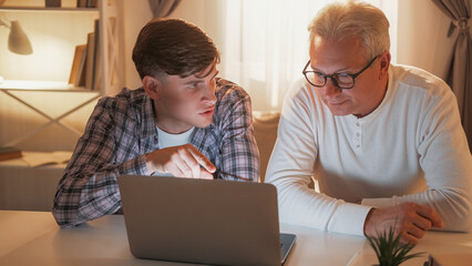Interesting movie. Family leisure. Curious father and son watching and discussing film together at laptop home interior.