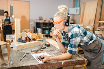 In the carpenter's shop, a professional woman crafts wooden furniture, using tools with skill in...