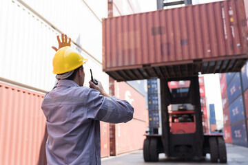 Portrait of male container yard worker loading containers box at commercial dock site. Male worker...