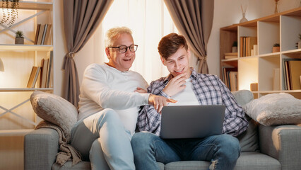 Internet booking. Family research. Online payment. Happy inspired father and son choosing holiday tickets on laptop together home room interior.