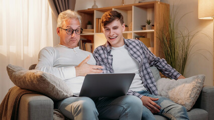 Online meeting. Family communication. Happy father and son talking by virtual call at laptop sitting sofa at room interior.