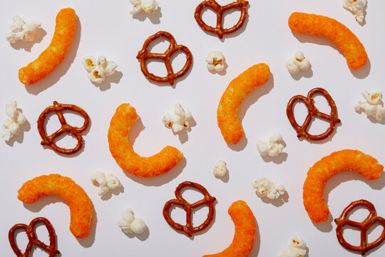 Overhead view of pretzels, cheese puffs and popcorn on white background
