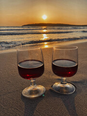 Two glasses of red wine stand on the sand on the beach. Scenic sunset over the sea. The sun goes below the horizon - Sardinia, Porto Pino