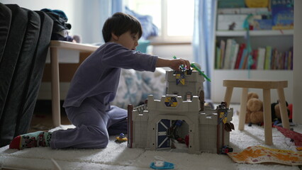 Small boy playing in bedroom with toy castle at home wearing pajamas. Child engrossed in...