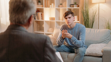 Psychology therapy. Male treatment. Mental health. Curious man listening psychologist on appointment session light room interior.