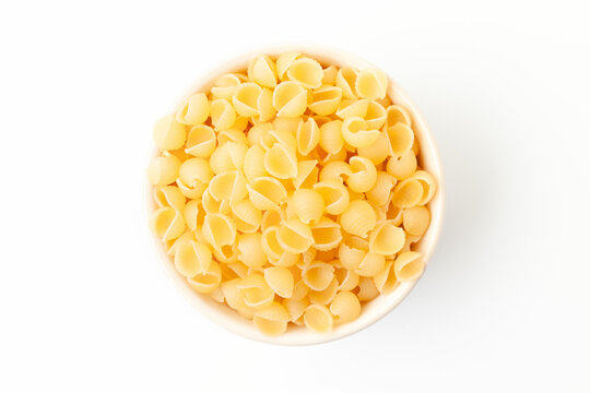 Yellow, small shell shaped pasta in bowl on white background. Top view - Powered by Adobe