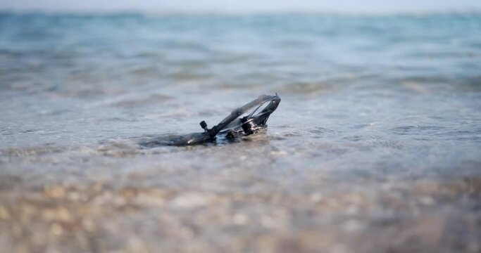 A close-up of the FPV drone, which lies on the coast in the ocean in the water. Found a drone on the beach, signal loss and breakdown. Drone crash.