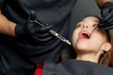 in a dental office male dentist gives an anesthetic injection to a young beautiful girl