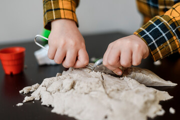 A small child plays in the sandbox at home. Boy makes sand molds