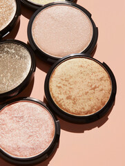 A variety of highlighter compacts cast shadows on a peach backdrop.