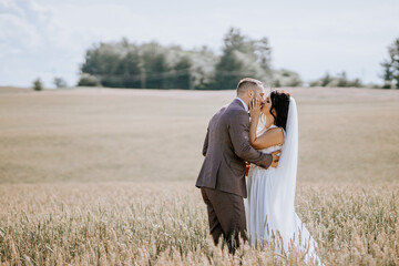 Valmiera, Latvia- July 28, 2024 - A bride and groom kiss in a wheat field, with a serene landscape...