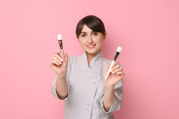 Cosmetologist with cosmetic brushes on pink background