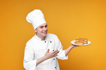 Portrait of happy confectioner in uniform holding plate with eclairs on orange background