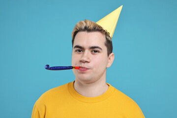 Young man with party hat and blower on light blue background