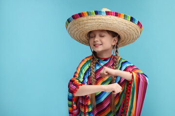 Cute girl in Mexican sombrero hat and poncho dancing on light blue background. Space for text