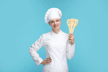 Happy chef in uniform holding wooden utensils on light blue background