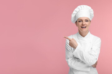 Happy chef in uniform pointing at something on pink background, space for text
