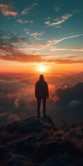 Obraz premium Man standing alone on a mountaintop overlooking a beautiful sunset