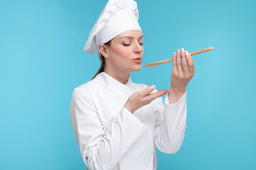 Woman chef in uniform tasting something on light blue background