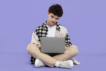 Portrait of student with laptop sitting on purple background