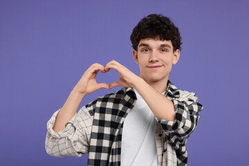 Happy young man showing heart gesture with hands on purple background
