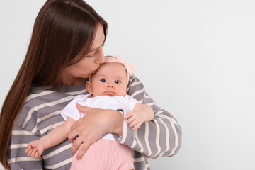 Mother kissing her cute baby on light background, space for text