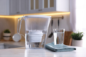 Water filter jug and glass on white marble table in kitchen, closeup