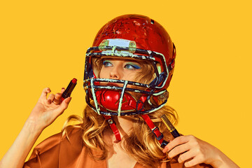 Portrait of woman in elegant attire wearing football helmet makes makeup against yellow studio background. Concept of woman in football, sport and fashion, style and beauty. Ad