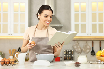 Young woman with recipe book cooking in kitchen